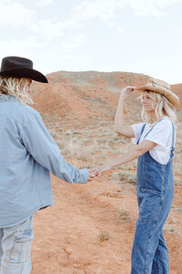 Two people who are engaged are holding hands while looking at each other in the desert 