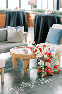 Modern wedding lounge setup with neutral seating, bold red and blush floral installation, and hand-lettered 'the best is yet to come' vinyl floor decal for a luxury wedding in Bozeman, MT.