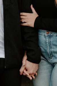 Close up of two people holding hands while also showing off an engagement ring