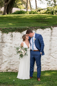 Bride and Groom kissing in front of a white washed wall