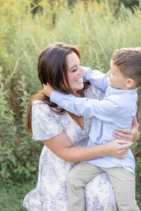 Candid moment of a mother and young son smiling at each other in a sunny field during a family photo session in Connecticut.
