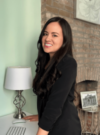 Young Latina professional in black blazer smiling and standing with arms on desk