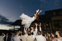 Guests tossing the bride into the air on the dance floor during a joyful wedding reception – documentary Colorado wedding photography