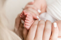 Close-up of a mother holding her newborn’s tiny toes in her hands, capturing the sweetness of early connection.