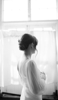 Person stands in wedding dress looking out window