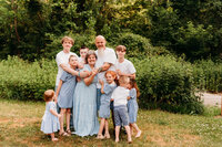 Grandmother and Grandfather surrounded by their 8 grandchildren.  Kids range in age from 2 through 17.  All are wearing different shades of blue and white to coordinate.  Photo taken by Philadelphia family photographer, Kristi
