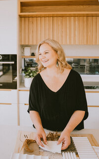 Personal brand image of confident female interior designer stood in beautiful, light filled kitchen.