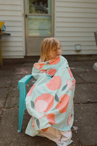 toddler girl sits in a small Adirondack chair wrapped in a large beach towel as she dries off on backyard patio
