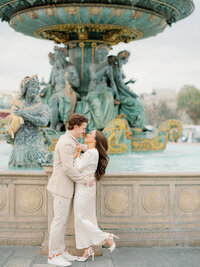 a man and woman standing in front of a large fountain facing each other and smiling