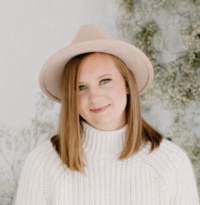 A woman sitting on a wood stool looking at the camera.