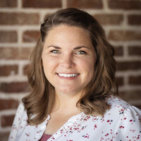 Jessica wearing a white blazer, smiling as she writes in her planner