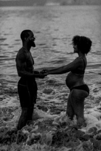 Vertical black and white image of couple standing in the ocean holding hands and laughing