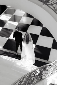 A bride and groom descend a grand checkered staircase, captured with a refined editorial wedding photography aesthetic.