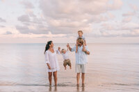 family of four standing in the ocean while laughing