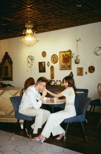 Fiance kissing his fiancee's hand during their coffee shop engagement session captured on film photography