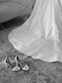 Black and white photo of a bride's dress and shoes on the floor