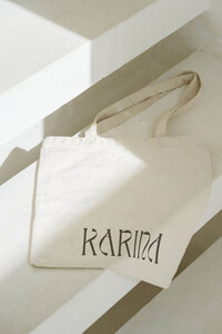Karina wellness Canva brand kit cotton tote bag mockup with minimalist logo, styled on sunlit concrete steps to evoke calm, natural, and intentional living.