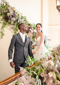 A groom beams during the first look on a stairway decorated with elaborate florals