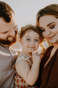 A mom and dad holding their toddler girl and resting their heads on her temple in fort worth, texas
