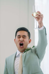 Best man in sage tuxedo tossing wine for the newly wed