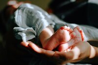 An adult cradles the feet of a newborn baby.