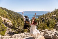 A wedding couple wearing backpacks jumps with Lake Tahoe in the background.