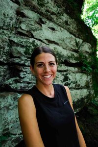 Mady Stoner in a black shirt stands confidently in front of a large rock.