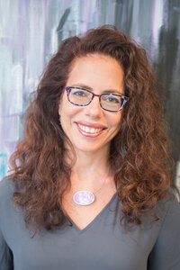 Jessica wearing a white blazer, smiling as she writes in her planner