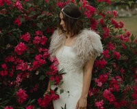 a bride in a flower bush. she is wearing ostrich feathers on her dress and a boho headpiece