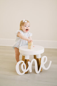 Baby girl in pink romper and bow smiles looking up with blue eyes sitting in moses basket during photo session