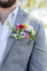 Man in grey suit with colorful flowers bulging out of pocket