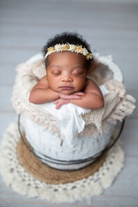 Boho newborn session with baby resting head on hands in a white bucket surrounded by rustic tones and lace