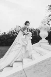 A bride wearing Monique Lhuillier wedding dress climbs stairs at a Rosecliff Mansion wedding