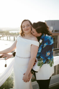 bride and bride on the terrace at La Vie at the Wharf in DC overlooking the anacostia river with bride kissing bride's neck