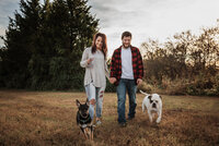 a man and woman walking two dogs and holding hands