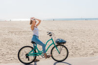 Best senior photographer in NJ. Picture of Nicole Marie Photography riding her bike in Venice beach, California. She is wearing blue Levi jeans and riding a blue beach cruiser while fixing her hair.