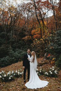 Bride and groom standing in the middle of an autumn covered forest smiling after their wedding ceremony