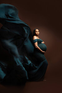 Dark Moody portrait of woman in flowing dress posing for maternity photography