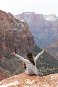 woman sitting on edge of canyon with arms above head