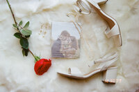 Film wedding detail picture of invitations, a red rose, and white heels.