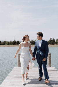 The groom and the bride are holding hands, smiling and walking on the pier,