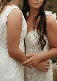 Close-up of brides’ hands and lace details of their dresses