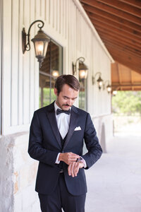 groom in tuxedo and bow tie looking at watch before ceremony at Milestone New Braunfels Texas by Firefly Photography