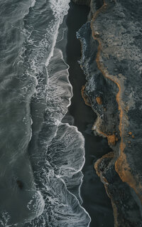 Black sand beach with frothy waves trying to reach the rocky shore