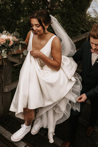 Groom helping bride with her dress as she walks up steps in Converse