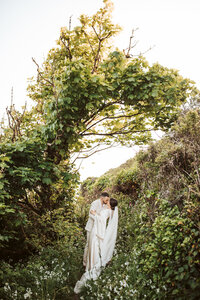 A couple kiss under a lush green arch made from a tree on the coast of looe england.