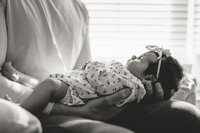 Intimate black and white portrait of dad holding newborn girl in front of window during in-home lifestyle newborn session 