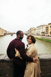 A couple hugs and smiles on Ponte Vecchio in Florence while posing for an engagement photoshoot