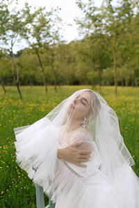 Fashion magazine portrait of bride with veil over her head in a field in Italy