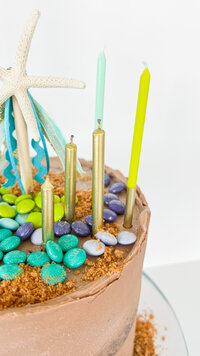 Close up image of birthday cake topped with candles and mermaid decorations.